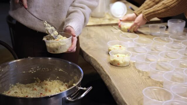 Close-up of a woman's hand picking rice porridge from large jar in plastic bowls to feed homeless people affected by russian-ukrainian war. The concept of help, volunteering, refugees