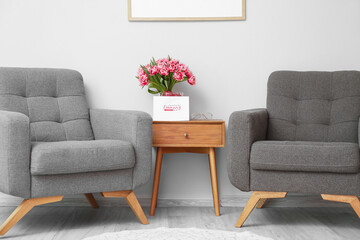 Armchairs and table with tulips and greeting card with text HAPPY WOMAN'S DAY near light wall
