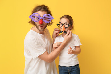Funny man and her little daughter in disguise on yellow background. April fools' day celebration