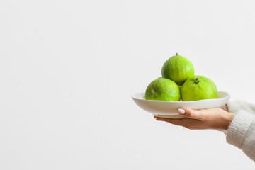 Woman holding plate with ripe bergamot fruits on light background