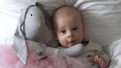 Close-up Happy playful kid 6 month old. Newborn boy looking at camera after bath shower on white soft bed. baby child waking time before bedtime with Toy. Childhood, motherhood, family, infant concept