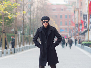 Portrait of handsome Chinese young man wearing black overcoat, sweater and trousers with sunglasses walking on Shanghai street, front view, male fashion, cool Asian young man lifestyle.