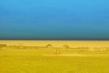 War Ukraine. Ukrainian flag. A tractor, farm machinery sprays insecticide a green corn wheat field with growth supplements and will destroy plant diseases. Agriculture. Providing food