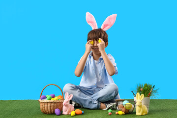 Adorable little boy with bunny ears and Easter eggs on blue background