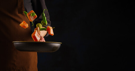 Pieces of red fish with vegetables in a frying pan in the hand of a professional chef. Levitation...