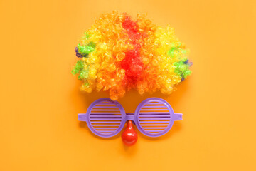 Composition with clown wig and eyeglasses on orange background. April Fools Day celebration