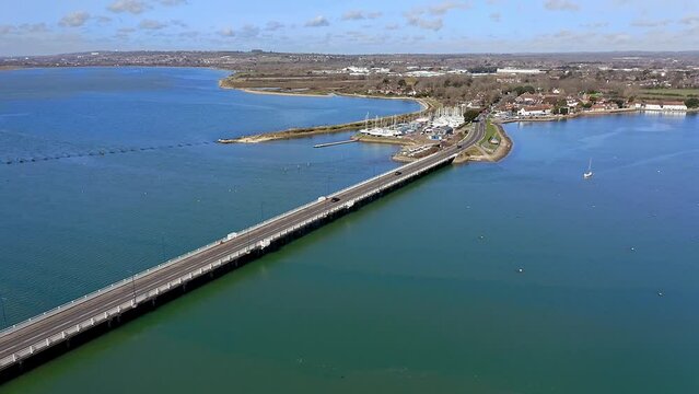 Langstone Bridge over Langstone Harbour which connects the mainland to Hayling Island, the Langstone Sailing Club is on the waterfront of the harbour, Aerial footage.