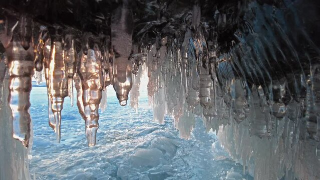 Ice cave on Baikal lake in winter. Blue ice and icicles in grotto in the sunset sunlight. Olkhon island, Baikal, Siberia, Russia, 4k