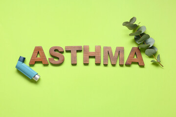 Composition with word ASTHMA made of wooden letters, inhaler and eucalyptus branch on green...