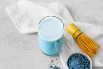Glass of blue matcha tea, chasen and bowl with powder on light background