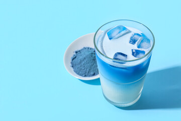 Glass of delicious matcha tea and bowl with powder on blue background