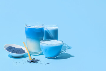 Glasses and cup of delicious matcha tea and bowl with powder on blue background