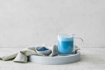 Glass cup of blue matcha tea and bowl with powder on light background