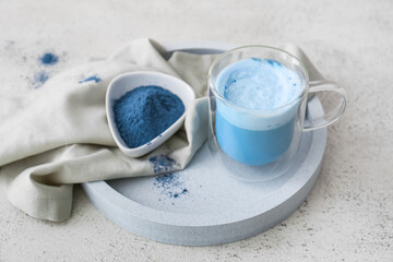 Glass cup of blue matcha tea and bowl with powder on light background