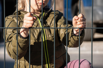 Child refugee hand holding a metal fence. Social problem of war migrants.