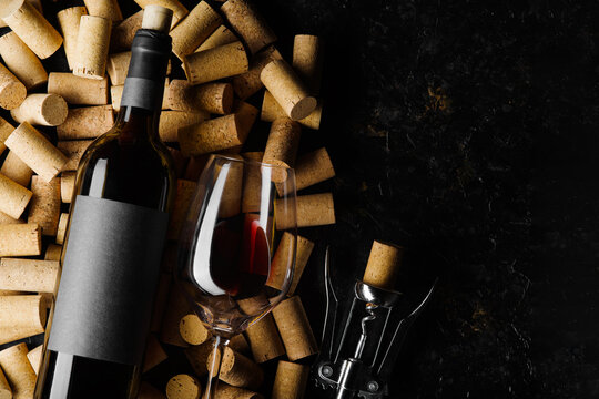 Festive composition. A bottle of red wine, a corkscrew and a wine glass lie on wine corks on a black background. There is free space to insert. Holiday, celebration, date, romantic evening. Banner.