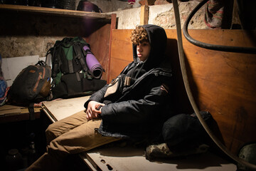 A teenager boy sits in the basement during the bombings in Ukraine. War. Russian aggression and...