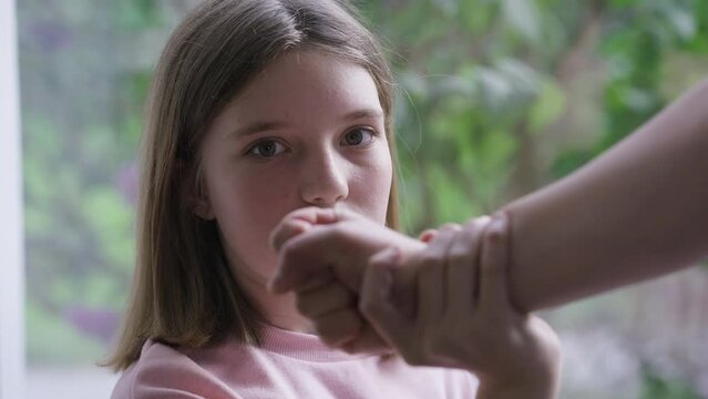 Close-up teenage girl stops fist punch attempt looking at camera with serious facial expression. Portrait of Caucasian teenager posing indoors. Family tyranny and child abuse concept