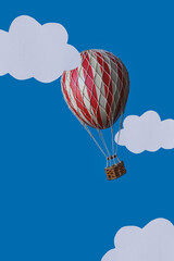 Hot air balloon travel concept. A red and yellow hot air balloon travels through the white clouds against a blue sky. Toy balloon and cut out clouds.