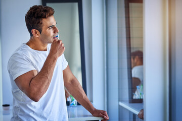 Deep in the morning routine zone. Shot of a handsome young man looking thoughtful while brushing his teeth at home.