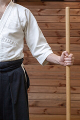 A man in a kimono and hakam stands in a stand-up in the hands of a wooden jo weapon