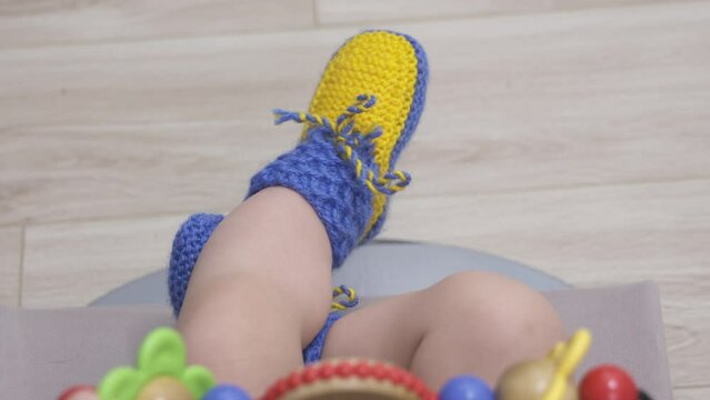 Baby dressed in homemade yellow blue knitted socks, tiny baby feet in woolen socks closeup. High quality 4k footage
