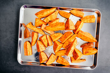 Raw Sweet Potato Wedges on a Sheet Pan: Uncooked sweet potato wedges seasoned with olive oil,...