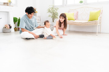 部屋で遊ぶ赤ちゃんとそれを見守る両親