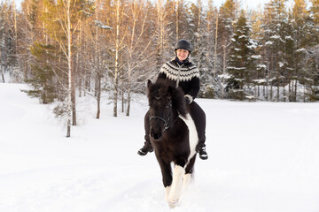 Icelandic horse ride in deep snow. Female rider with Icelandic sweater and helmet.