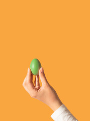 Green colored Easter egg in beautiful woman's hand against orange background. Retro aesthetic style.