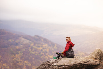 Fototapeta premium Hiker girl taking a rest on a rock in the mountains. Windy day. Travel and healthy lifestyle outdoors in fall season