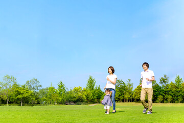 青空を背景に緑の芝の上で一緒に走る幸せな娘と若いカップル。家族,幸せ,愛情,育児のイメージ