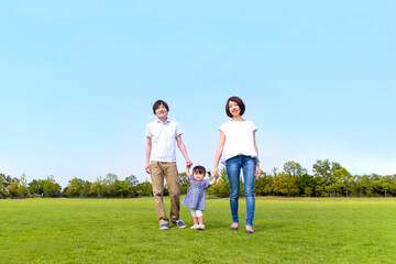 Obraz premium 青空を背景に緑の芝の上で手を繋ぐカメラ目線の幸せな娘と若いカップル。家族,幸せ,愛情,育児のイメージ