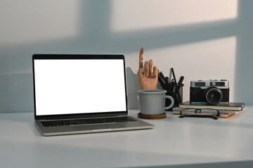 White modern office table with laptop with blank white screen, camera, coffee cup and note books with no people, for business and technology concept.