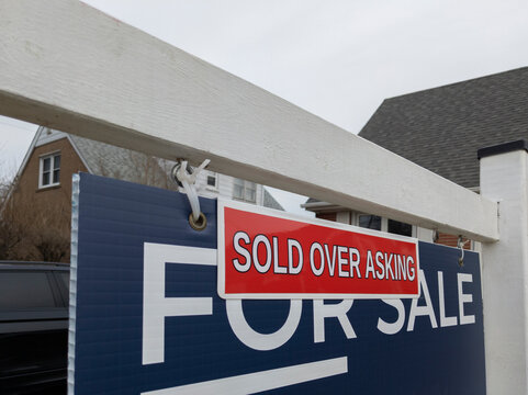 Sign sold over asking price  in front of a detached house in residential area. Real estate bubble, hot housing market, overpriced property, buyer activity, spring and summer sale concept.