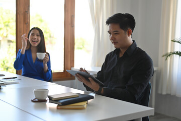 A portrait of happy Asian businesswoman taking a break in the office and the man is working very serous on a tablet, for business, technology, finance and insurance concept.