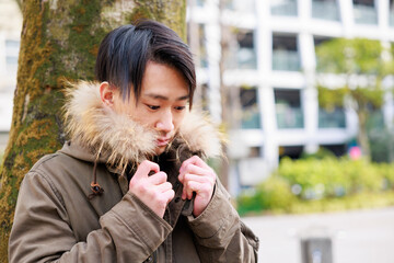 公園の木の近くで寒そうにコートを着る日本人男性