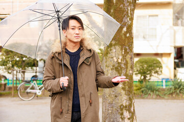 公園で傘をさしている日本人男性