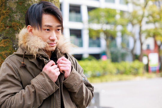 公園の木の近くで寒そうにコートを着る日本人男性