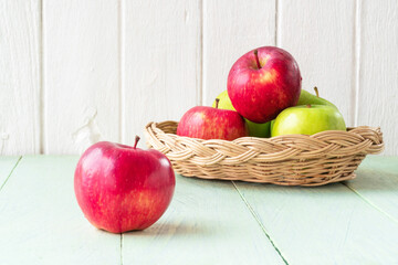 Red apple and apple fruits in basket on wooden floor.
