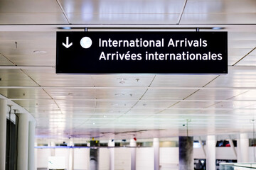 International arrivals sign board in english and french at airport terminal hall. Canada government...