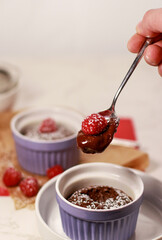 spoon with chocolate lave cake with raspberry in a purple ramekin, blurred background
