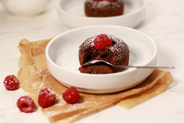 close up of chocolate lave cake on a white plate with raspberries, white marble table