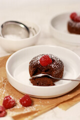Close up of chocolate lave cake on a white plate with raspberries, white marble table