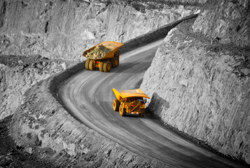 Two trucks in a modern gold mine in Australia. Spot colour large haul trucks transport gold ore from the pit, Opencast mine. Yellow trucks, black and white background. - All logos removed. - obrazy, fototapety, plakaty