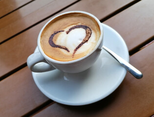 coffee with milk in a white cup decorated with a heart on a bar table.