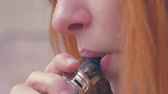 Close-up of a woman with red hair smoking electronic cigarette outdoor