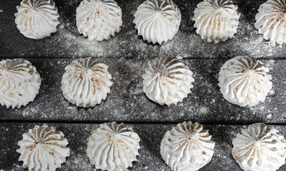 Culinary background with vanilla meringue on dark wooden background, sprinkled with nuts, cocoa and powdered sugar. Still life in style of food. Sweet meringue, delicious and light dessert.