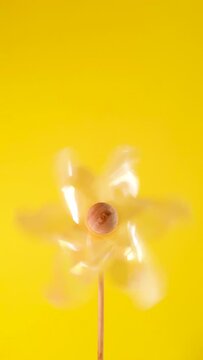 One yellow plastic pinwheel windmill spinning fast on vibrant yellow blurred background. Vertical windenergie alternative energy and kids relax garden toys concept with copy space