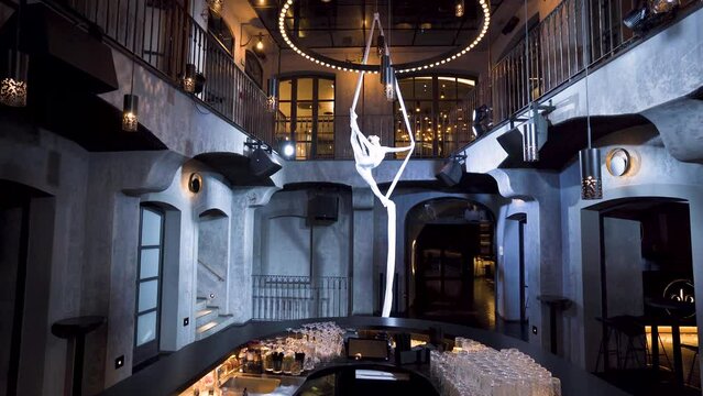 Female aerialist doing spinning pench&eacute; split on silks in a music club.